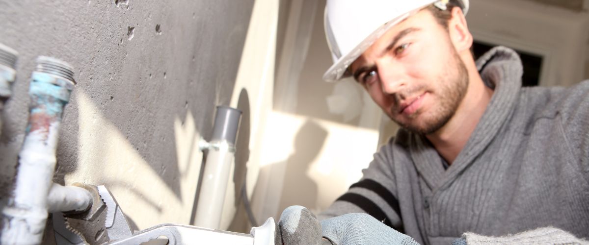 Plumber repairing pipes in a home, focusing on plumbing maintenance and emergency repairs related to burst pipes.