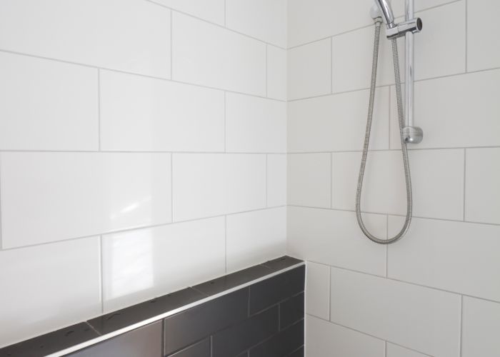 Shower installation with sleek white tiles and modern handheld showerhead, emphasizing a clean and efficient bathroom setup for tankless water heater use.