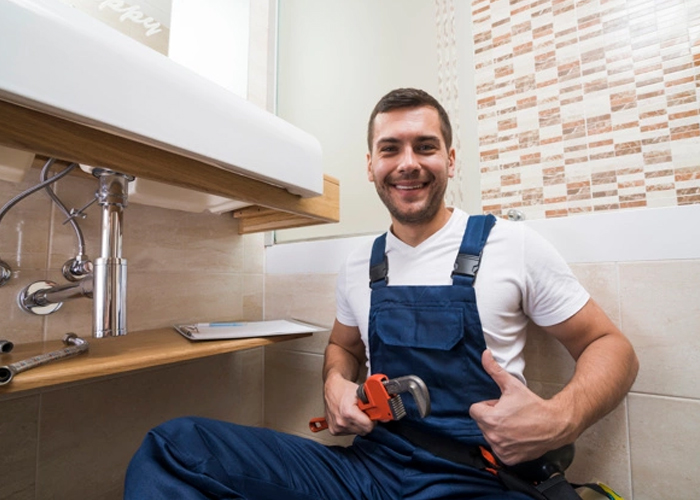 Plumber in blue overalls working under a modern bathroom sink in Bordentown, NJ.