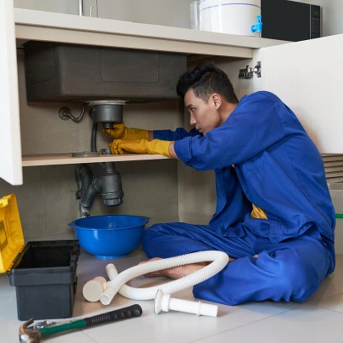 Plumber in blue uniform inspecting under-sink drainage during plumbing repair services in Bordentown, NJ.