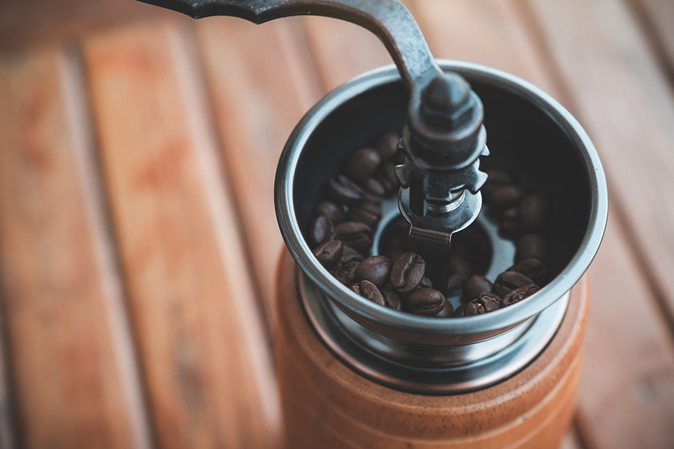 Coffee grinder with whole coffee beans, emphasizing the importance of proper disposal of coffee grounds to prevent drain clogs.