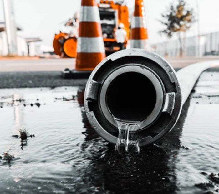 Sewer pipe leaking water with construction cones in the background, illustrating sewer line repair and maintenance services by Alliance Service Pros.