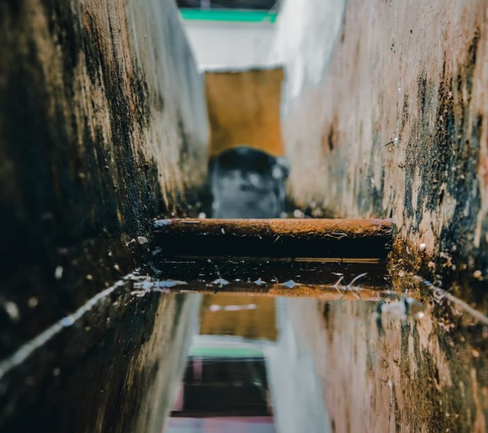 Sewer line with standing water and rusted pipe, illustrating sewer issues related to blockages and potential repairs needed.