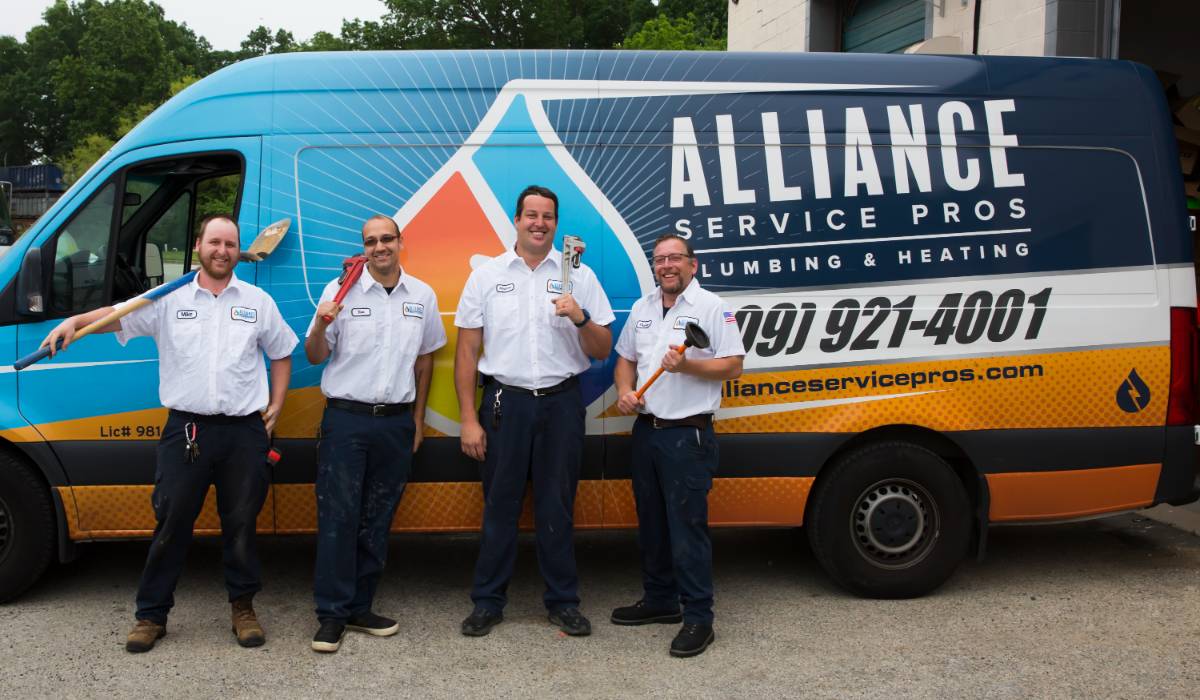 Four plumbers from Alliance Service Pros standing in front of a branded service van, holding plumbing tools, showcasing their expertise in toilet leak repair and installation services in New Jersey.