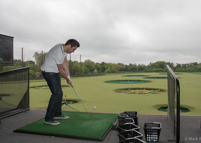 Man swinging golf club at Topgolf driving range in Mount Laurel, NJ, with green targets in the background.