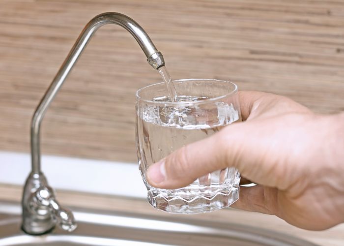 Hand holding a glass under a water filtration faucet, filling it with clean, filtered water.