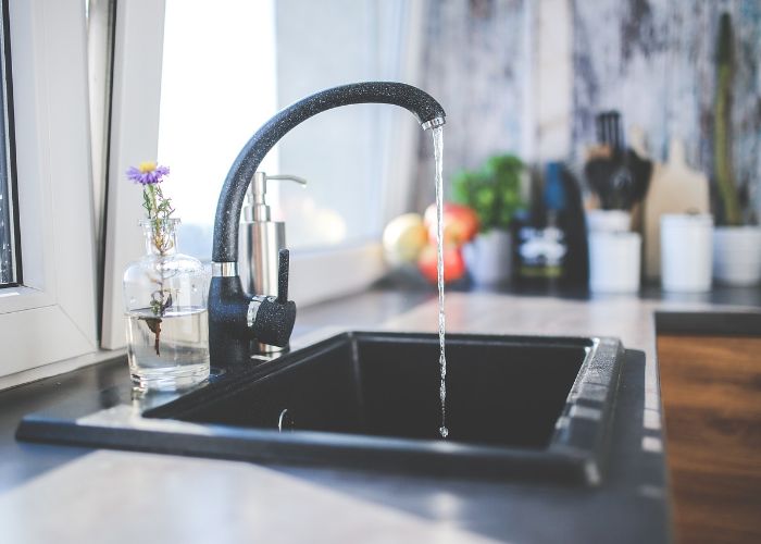 Modern kitchen faucet with running water over a black sink, showcasing home water filtration benefits and the importance of clean drinking water.