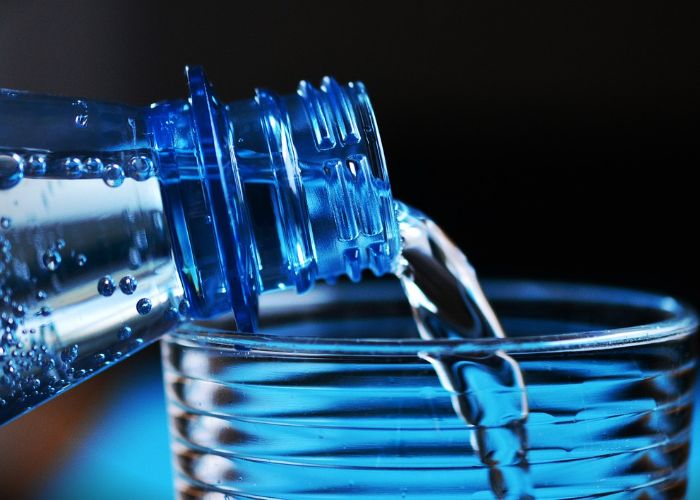 Water being poured from a blue plastic bottle into a clear glass, highlighting the importance of clean, filtered drinking water.