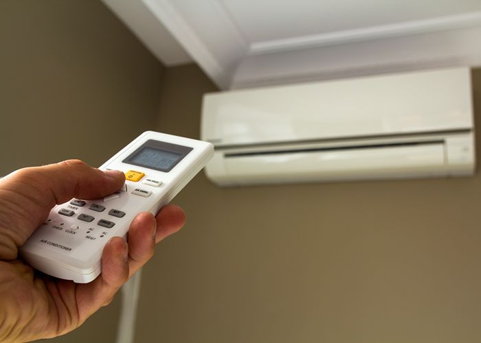 Hand holding a remote control aimed at a wall-mounted ductless mini split air conditioning unit, illustrating HVAC installation and operation in New Jersey.